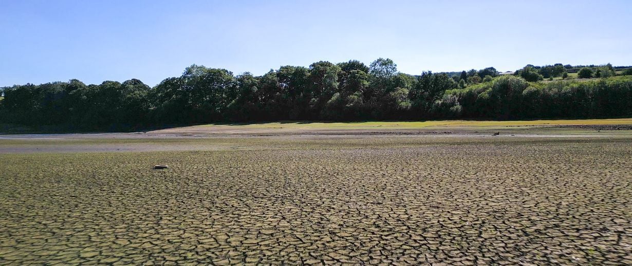 Drone footage of aerial view over a British reservoir, during drought in summer 2022 heatwave. Empty reservoir basin shows cracked dry bare ground.