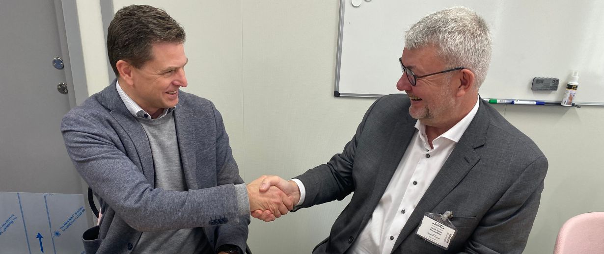 Two business people shake hands after signing a contract that sits on a table in front of them