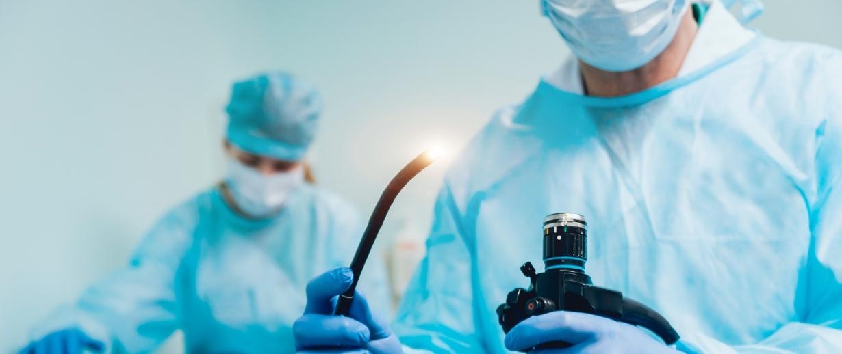 A medical worker in uniform holding an endoscope toward the camera