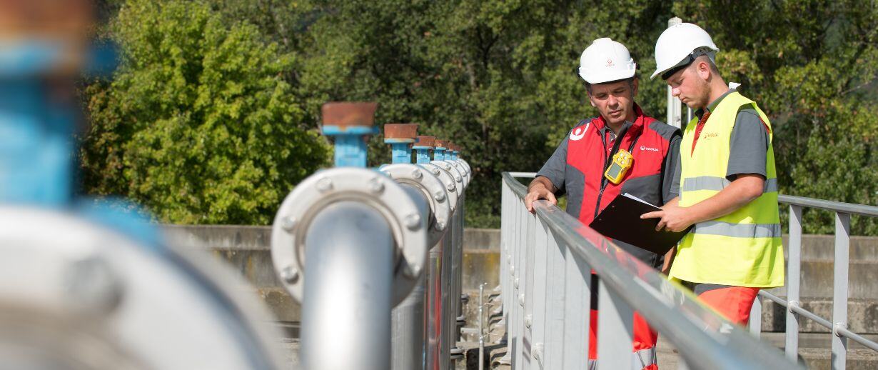Two water treatment engineers PPE talking on a metal bridge